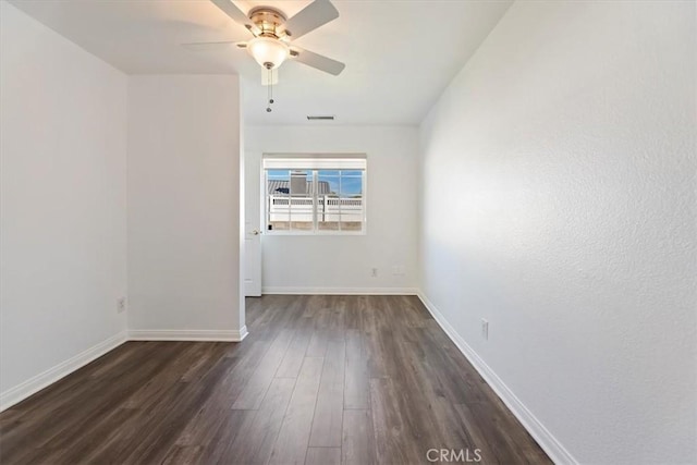 unfurnished room featuring dark wood-style floors, a ceiling fan, visible vents, and baseboards