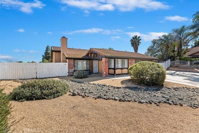 view of front facade with a fenced front yard, a chimney, and a tiled roof