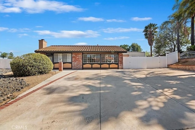 single story home with brick siding, fence, a tiled roof, a gate, and a chimney