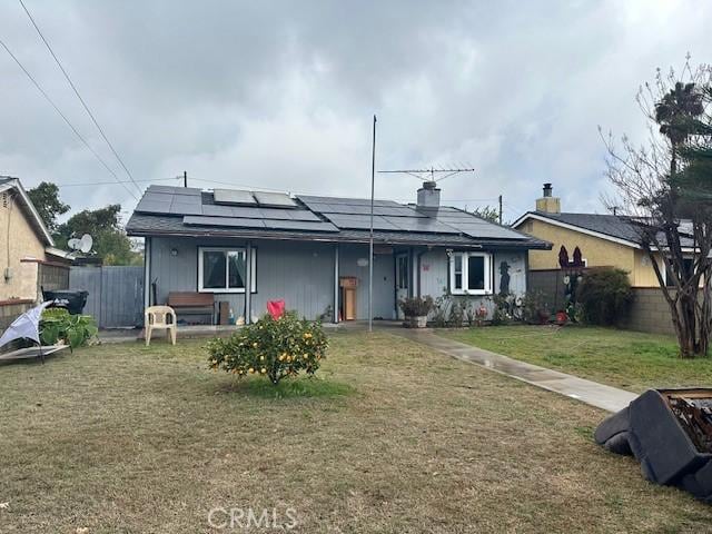 view of front of property with fence, solar panels, and a front yard