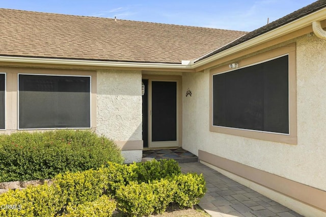 entrance to property with stucco siding and roof with shingles