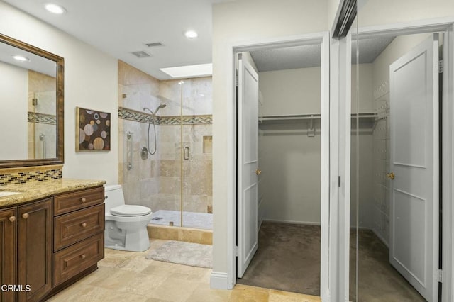 bathroom featuring vanity, a shower stall, a walk in closet, toilet, and backsplash