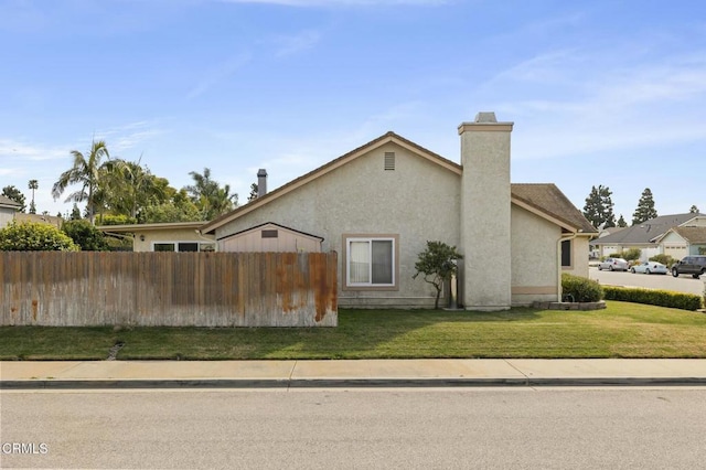 view of home's exterior with a chimney, fence, a lawn, and stucco siding