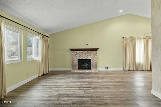 unfurnished living room with lofted ceiling, a brick fireplace, wood finished floors, and baseboards