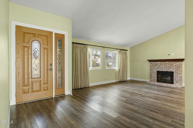 foyer with vaulted ceiling, a brick fireplace, wood finished floors, and a textured ceiling