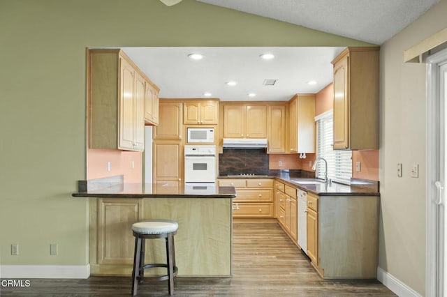 kitchen with white appliances, vaulted ceiling, under cabinet range hood, and light brown cabinetry