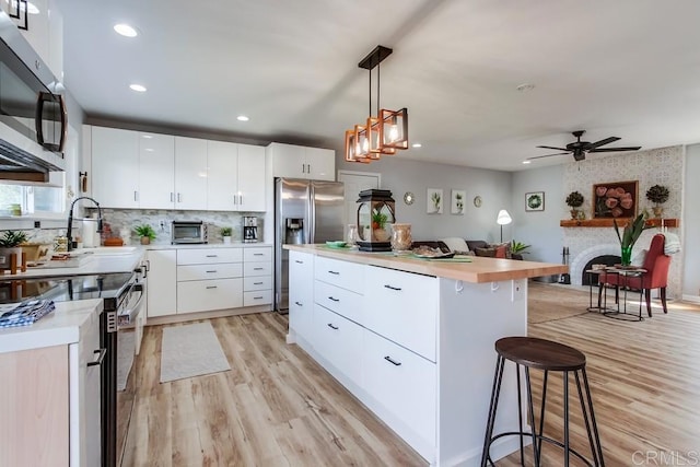 kitchen with appliances with stainless steel finishes, white cabinets, a large fireplace, pendant lighting, and a center island