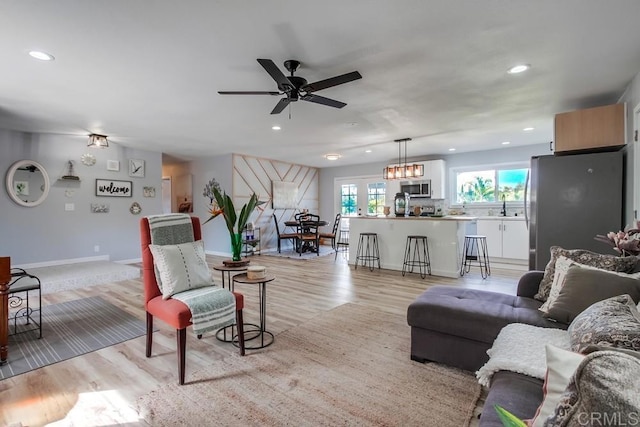 living room with light wood-type flooring, sink, and ceiling fan