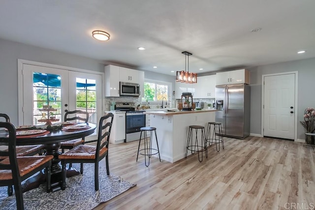 kitchen with appliances with stainless steel finishes, hanging light fixtures, french doors, and white cabinets