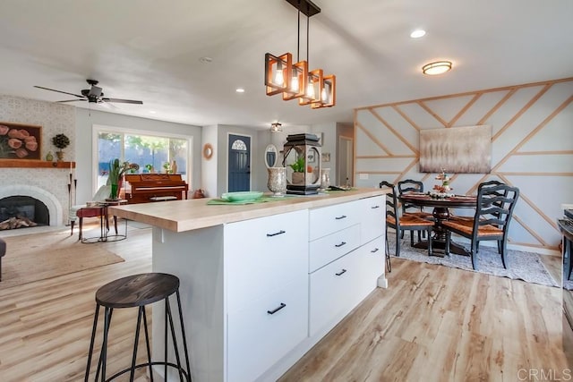 kitchen featuring hanging light fixtures, light hardwood / wood-style floors, a large fireplace, a kitchen island, and white cabinetry