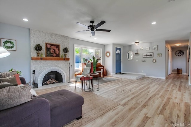 living room with a large fireplace, ceiling fan, and light hardwood / wood-style flooring