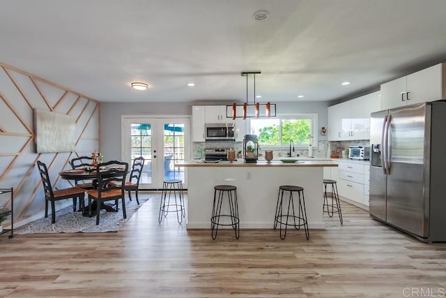 kitchen featuring french doors, a breakfast bar, appliances with stainless steel finishes, white cabinets, and pendant lighting