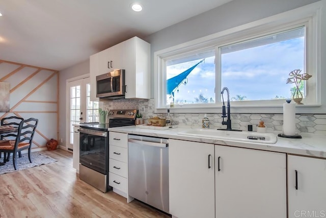 kitchen featuring light wood-type flooring, stainless steel appliances, white cabinets, backsplash, and sink