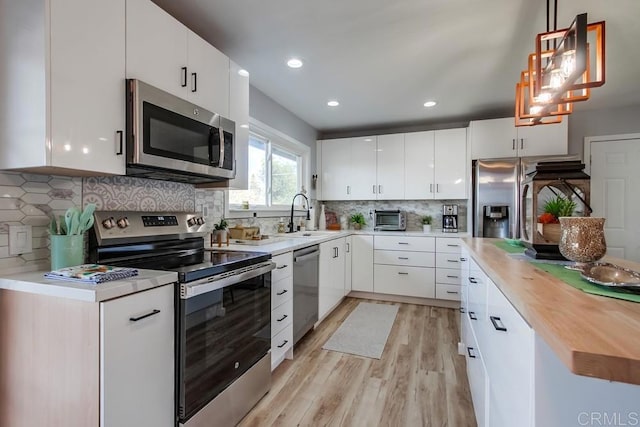 kitchen with decorative light fixtures, sink, stainless steel appliances, and white cabinetry