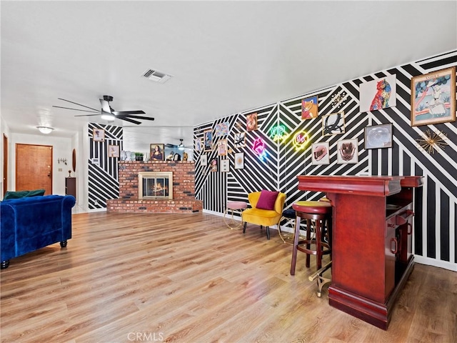 game room featuring ceiling fan, light wood-type flooring, and a brick fireplace