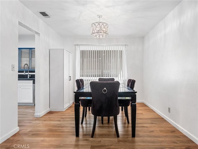 dining space with sink, light wood-type flooring, and a chandelier