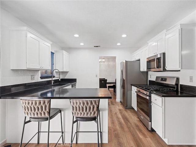 kitchen with sink, white cabinetry, stainless steel appliances, kitchen peninsula, and a breakfast bar area