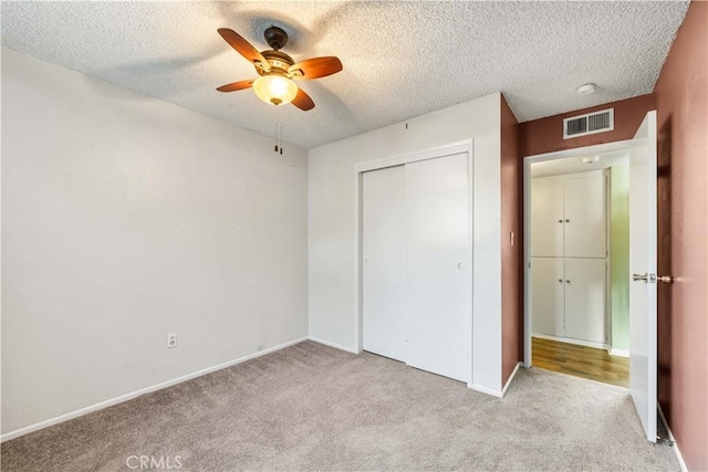 unfurnished bedroom featuring a textured ceiling, light carpet, and a closet