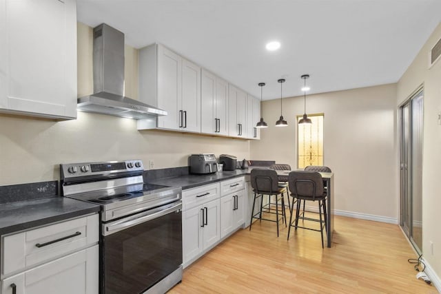 kitchen featuring decorative light fixtures, wall chimney range hood, light hardwood / wood-style floors, white cabinets, and stainless steel range with electric cooktop