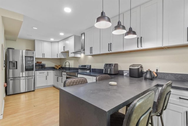 kitchen with a kitchen bar, white cabinetry, decorative light fixtures, wall chimney range hood, and stainless steel appliances