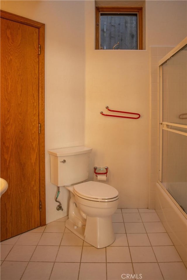 bathroom with toilet, tile patterned flooring, and bath / shower combo with glass door