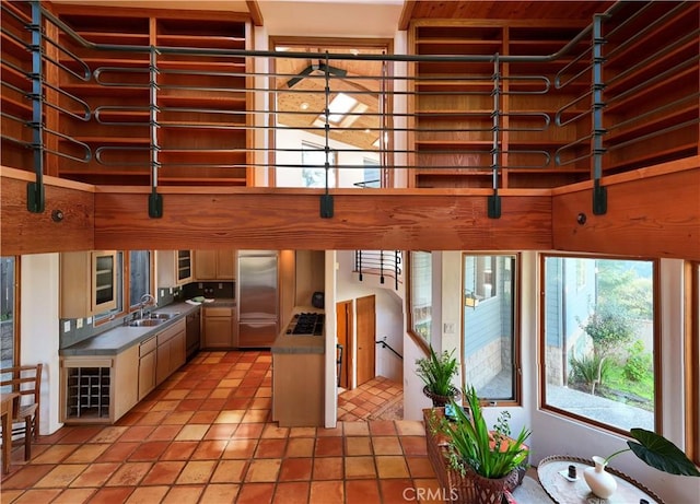 kitchen featuring light tile patterned floors, stainless steel appliances, hanging light fixtures, a towering ceiling, and a sink