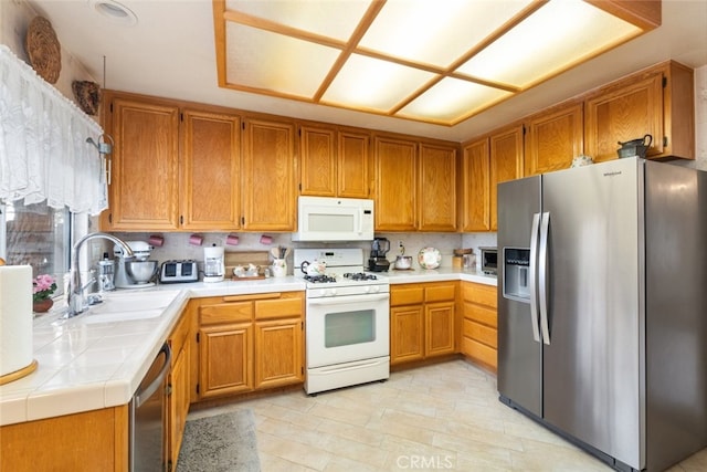 kitchen with tile countertops, appliances with stainless steel finishes, a sink, and brown cabinets