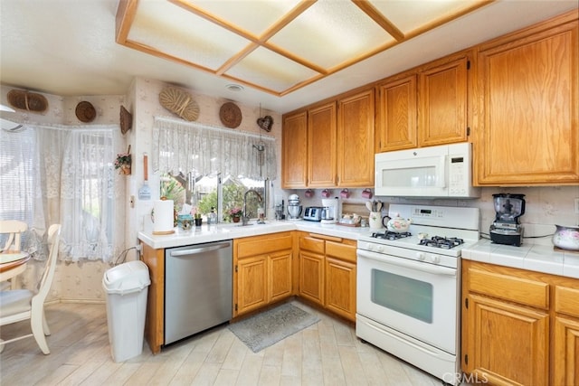 kitchen featuring tile countertops, light wood finished floors, brown cabinetry, a sink, and white appliances