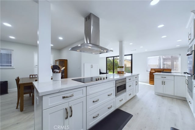 kitchen featuring island range hood, stainless steel appliances, white cabinets, and light stone counters