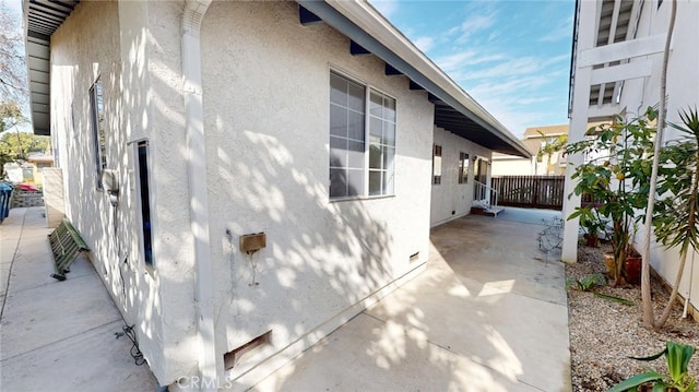 view of side of home with crawl space, a patio area, fence, and stucco siding