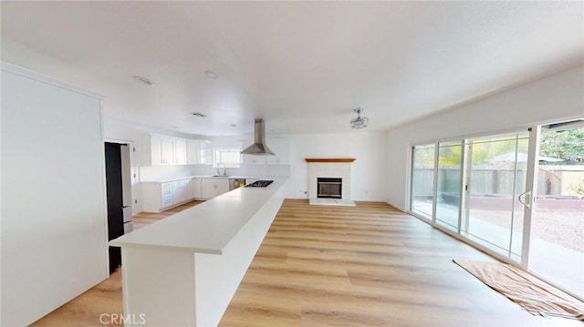 kitchen with light countertops, white cabinets, a sink, island range hood, and a peninsula