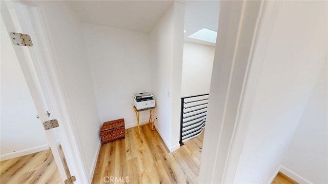 hall with baseboards, a skylight, an upstairs landing, and light wood-style floors