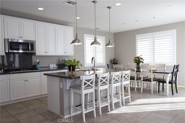 kitchen featuring stainless steel microwave, visible vents, a kitchen island with sink, white cabinets, and black electric cooktop