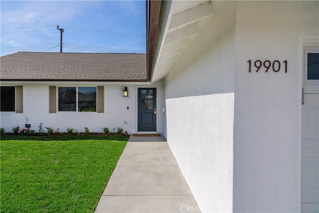 entrance to property with a yard, a shingled roof, and stucco siding