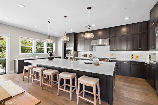 kitchen featuring a kitchen island with sink, hanging light fixtures, light hardwood / wood-style flooring, a kitchen bar, and decorative backsplash