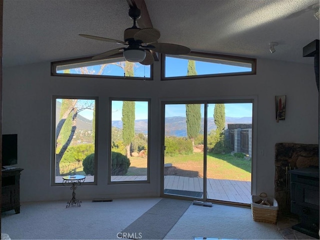 unfurnished living room featuring a textured ceiling, a wood stove, light colored carpet, and lofted ceiling