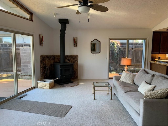 carpeted living room featuring ceiling fan, vaulted ceiling, a wood stove, and a textured ceiling