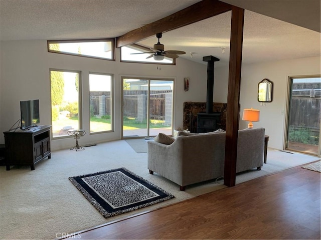 living room featuring a wood stove, ceiling fan, lofted ceiling with beams, a textured ceiling, and wood-type flooring