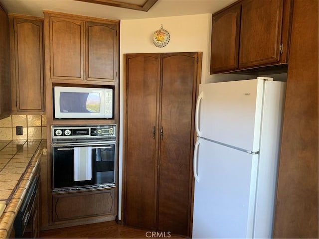 kitchen with tile countertops, white appliances, and tasteful backsplash