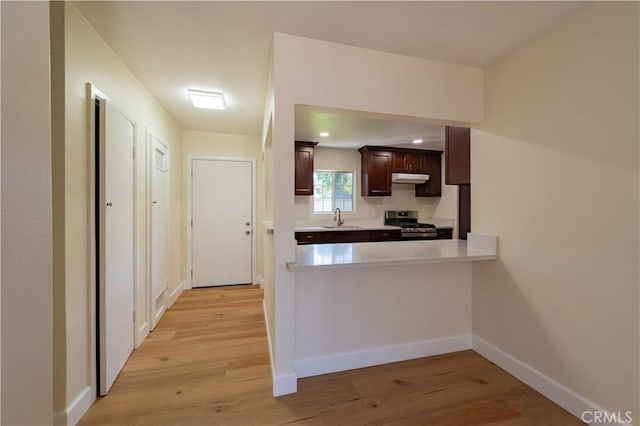 kitchen with light wood-type flooring, kitchen peninsula, dark brown cabinetry, sink, and stainless steel range