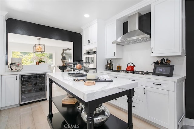 kitchen with beverage cooler, white cabinetry, stainless steel appliances, wall chimney exhaust hood, and hanging light fixtures