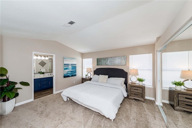 bedroom with lofted ceiling, connected bathroom, and light colored carpet