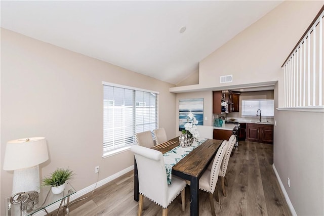 dining area featuring light hardwood / wood-style floors, high vaulted ceiling, and sink