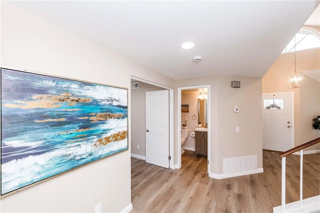 hall featuring light hardwood / wood-style floors, a chandelier, and lofted ceiling