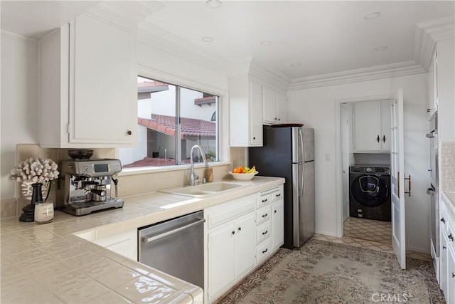 kitchen featuring tile counters, washer / clothes dryer, appliances with stainless steel finishes, white cabinets, and a sink