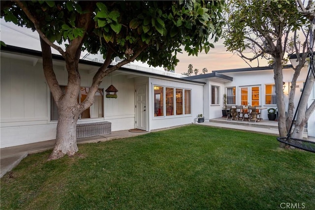 rear view of property with a lawn, a patio area, and stucco siding