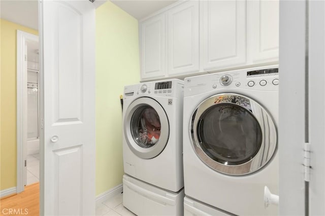 clothes washing area with washer and dryer, cabinets, and light tile patterned flooring