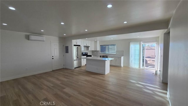 kitchen with appliances with stainless steel finishes, light hardwood / wood-style flooring, a center island, a wall unit AC, and white cabinets