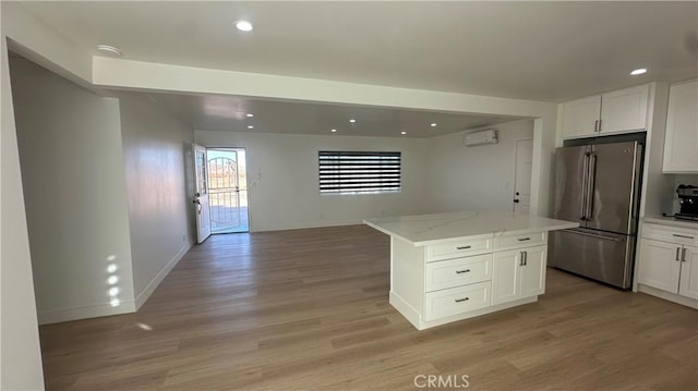 kitchen with high end fridge, an AC wall unit, light stone countertops, white cabinets, and a center island