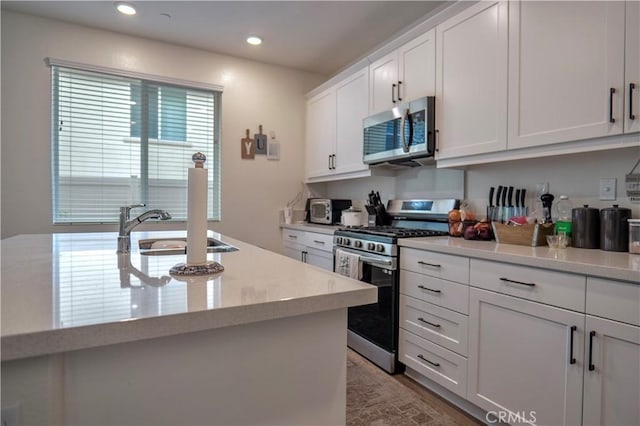 kitchen with appliances with stainless steel finishes, sink, white cabinets, light stone countertops, and a kitchen island with sink